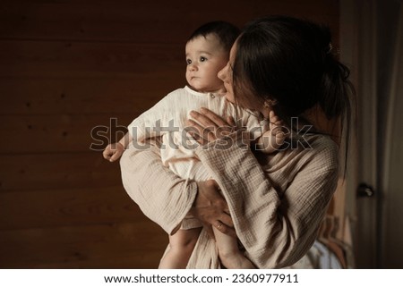 The Joys of At-Home Parenting: A Glowing Mom Lovingly Kisses Her Toddler, Both Draped in Earthy Muslin Comfortwear, Inside Their Rustic Abode