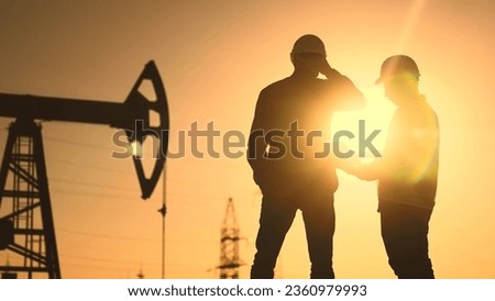 oil production. two silhouette workers work as a team next to an oil pump. business oil production production concept. two engineers of the oil and gas industry are sun discussing business plan Royalty-Free Stock Photo #2360979993