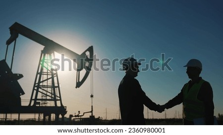 handshake business oil contract. handshake worker and businessman shaking hands against backdrop of an oil pump sunlight. oil extraction business concept. silhouette handshake business contract Royalty-Free Stock Photo #2360980001