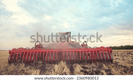 Agriculture. tractor plows field of black soil against the background of blue clouds. lifestyle agriculture business industry concept. plow machine tractor farm cultivates the soil after harvest Royalty-Free Stock Photo #2360980013