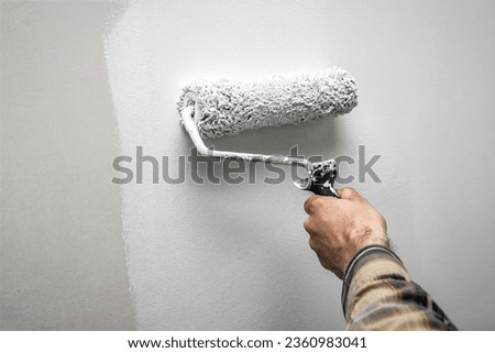 Hand Holding a Paint Roller While Painting a House Wall. Industrial theme