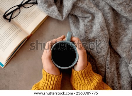people, season and leisure concept - person drinking black coffee and reading book at home in autumn Royalty-Free Stock Photo #2360989775