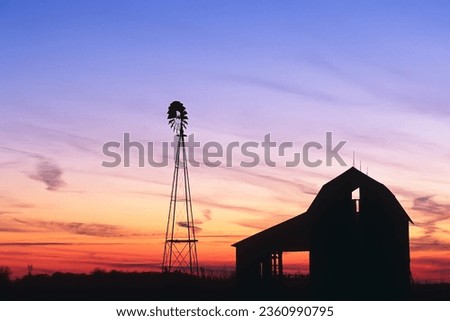 A beautiful sunset of a windmill and barn silhouetted against the evening sky in rural Indiana USA, North America Royalty-Free Stock Photo #2360990795