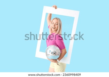 Young beautiful happy woman with frame and disco ball on blue background