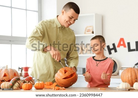 Little boy with his father carving Halloween pumpkin in kitchen