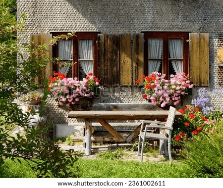 a traditional Bavarian country house covered with wood shingles with lush geraniums on the window ledge in the Bavarian Alps on a warm day in September, Oberjoch, Bad Hindelang, Bavaria, Germany       Royalty-Free Stock Photo #2361002611
