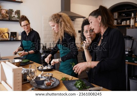 group of cooks, friends or colleagues cut ingredients cook together and prepare dinner at a wooden table in a kitchen or restaurant Royalty-Free Stock Photo #2361008245