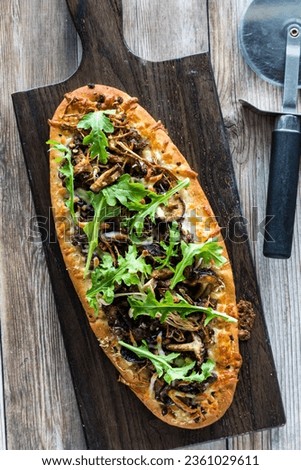 Top down view of a homemade mushroom beef flatbread pizza topped with arugula. Royalty-Free Stock Photo #2361029611