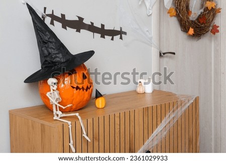 Halloween pumpkins with skeleton and candles on commode in hall