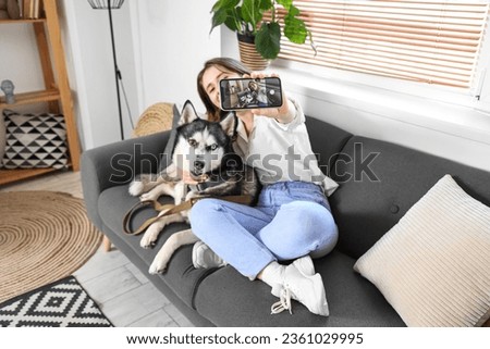 Happy young woman with husky dog taking selfie at home