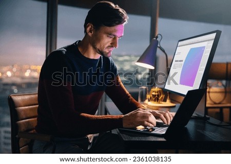 Caucasian businessman sits at his desk in an office at night, using a laptop for market analysis and research. Professional man working late hours, typing with determination to meet the deadline. Royalty-Free Stock Photo #2361038135