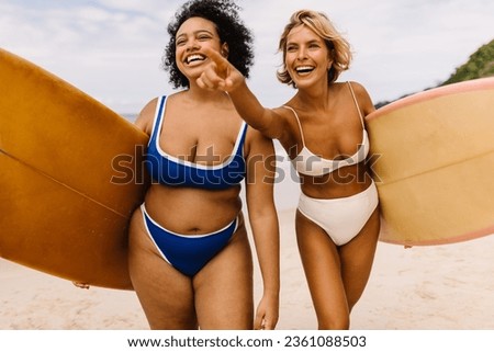 Excited female surfers going to a fun surfing spot on the beach, anticipating a happy and memorable surfing session. Two sporty women walking on shore in bikinis, eager to catch the best waves. Royalty-Free Stock Photo #2361088503