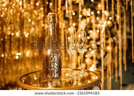 Champagne bottle with golden sequin and glasses at sparkling bokeh yellowish garlands blaze. Bright falling gold glitter ribbons backdrop glistening twinkle decoration for celebrating luxury party