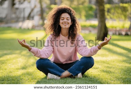 pretty young curly woman making digital detox in park meditating, having peace time for tranquility and mindfulness, relaxing sitting on grass in summer Royalty-Free Stock Photo #2361124151