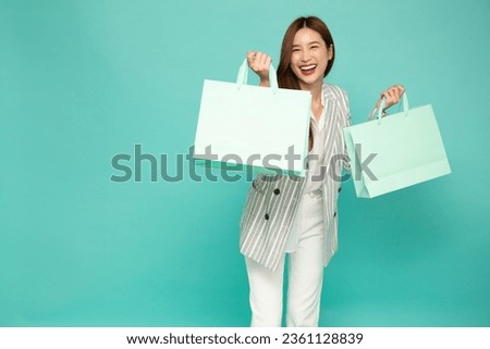Young beautiful Asian woman smiling and holding paper shopping bag isolated on green background, Supermarket and fashion mall concept Royalty-Free Stock Photo #2361128839