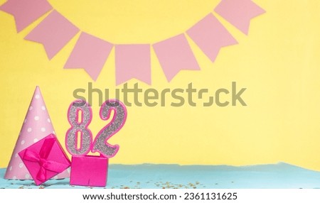 Date of birth for a girl  82. Copy space. Birthday in pink shades with a yellow background. Decorations with numbered candles and a gift box. Anniversary card for a woman