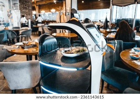 Robot waiter serve food at modern restaurant table.Offering innovation futuristic high-tech automated dining experience.Bringing,delivery automation order to customer.Digital robotic AI smart service. Royalty-Free Stock Photo #2361143615