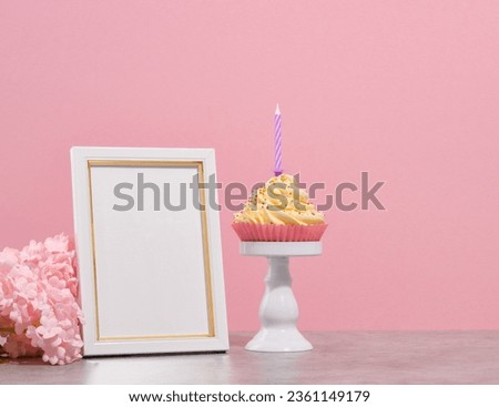 Holiday cupcake with colored sprinkles and a candle on a white stand. White photo frame. Holiday flowers. Copy space for text.