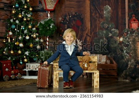 Cute child, holding suitcase and teddy bear, waiting at home for holidays, studio shot