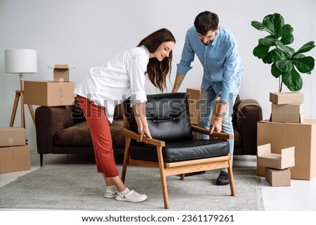 Smiling couple carrying modern chair together, arranging furniture, moving into new flat. Home improvement interior design, furnishing living room, renovation and refurbishment Royalty-Free Stock Photo #2361179261