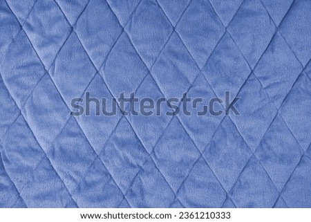 Quilted velours fabric background. Blue texture blanket or puffer jacket, stiched with diamond pattern, soft wrinkled surface, crupmed textile