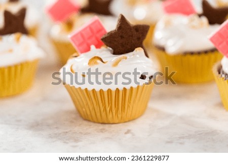 Gourmet s'mores cupcakes with meringue frosting and garnished with star-shaped chocolate graham cracker and a mini pink chocolate bar.