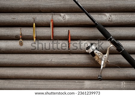 spinning wheel and rod with coourful lures hanging on a grey  wall of wooden stocks