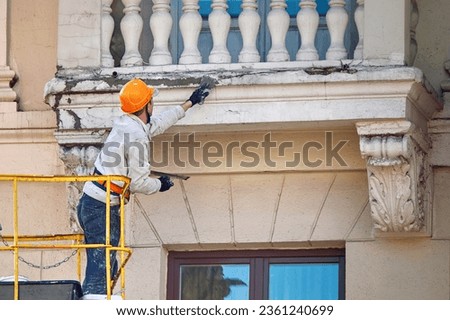Worker in cradle repairing balcony, plastering cracked stucco with trowel, renovation work, restore facade of historic building. Plaster cladding and crack repair. Plasterer repair balcony of building Royalty-Free Stock Photo #2361240699
