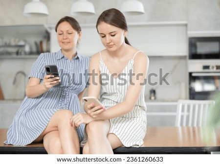 Joyful mother with adult daughter write messages in instant messengers on smartphones at home Royalty-Free Stock Photo #2361260633