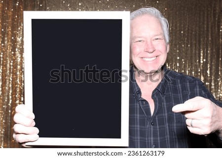Photo Booth. A man smiles as he holds a blank Black sign while having his pictures taken in a Photo Booth. Blank Sign. Room for text or images. Photo Booth Sign. Wedding Photo Booth. Party Time. Fun 