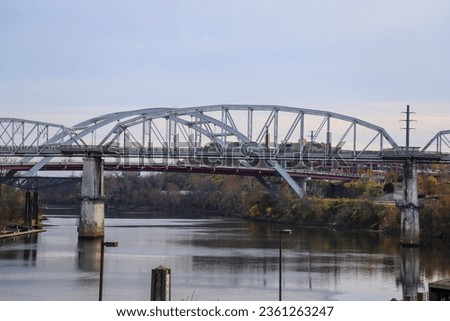 a gorgeous autumn landscape along the Cumberland River with the John Seigenthaler Pedestrian Bridge over the water, blue sky and clouds in Nashville Tennessee USA Royalty-Free Stock Photo #2361263247