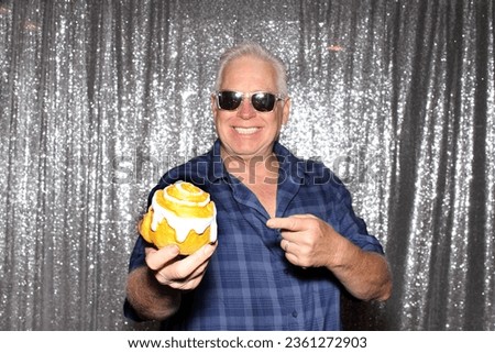 Photo Booth. FOOD. A man smiles and enjoys a Cinnamon Roll while having his picture taken in a Photo Booth at a Wedding or Party. People love Photo Booth almost as much as their Lunch or Dinner. 
