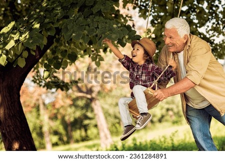 Grandfather and grandson playing in a park with a swing Royalty-Free Stock Photo #2361284891
