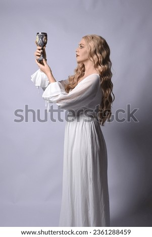 Close up portrait of beautiful blonde model wearing elegant  white halloween gown, a historical fantasy character.  Holding wine goblet, isolated on audio background.