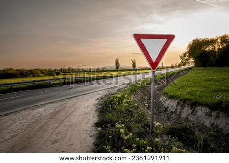 Selective blur on a european yield roadsign, a sign indicating a car doesn't have the priority over a road, at sunset, dusk, in a serbian countryside of vojvodina.