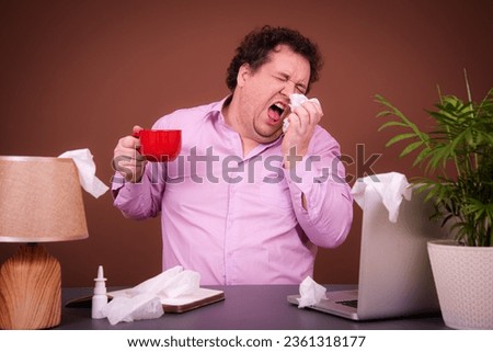 Flu and epidemic, businessman with a cold. Funny fat man posing at a table with a laptop. Brown background. Royalty-Free Stock Photo #2361318177