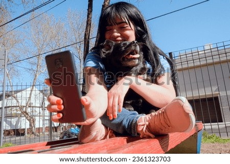 young latin woman sitting with her dog in park in afternoon, sending selfie photo with her phone to her pet's vet, people and animals concept, copy space
