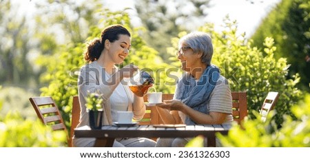 Happy young woman and her mother drinking tea in summer morning. Family sitting in the garden with cups and enjoying the conversation. Royalty-Free Stock Photo #2361326303