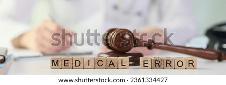 Words medical errors collected from wooden cubes with judge's gavel on table, doctor with stethoscope in background. Malpractice, medical error and investigation concept. Royalty-Free Stock Photo #2361334427