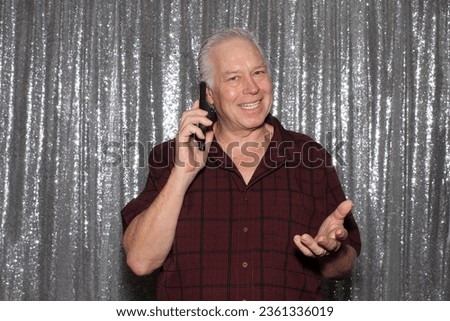 Photo Booth. A man smiles as he talks on his phone while waiting for his pictures to be taken while in a Photo Booth at a Wedding. Photo Booths are popular at Weddings, and all events. Cell Phone.