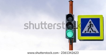 A pedestrian crossing sign with a reflective coating and a traffic light is installed on the street next to the school and warns drivers about the pedestrian crossing. Be careful on the road