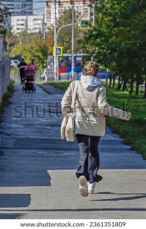 A woman runs along the sidewalk on an autumn day Royalty-Free Stock Photo #2361351809