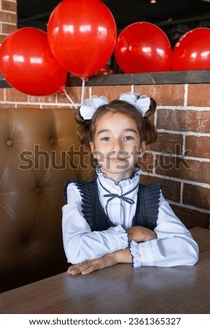Portrait of a girl student of the 1st grade school with white bows in a dress unifor at the school desk. Back to school, September 1, First - grade. Primary education, elementary class.  Royalty-Free Stock Photo #2361365327