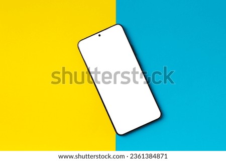 Smartphone with white screen on a bright two-tone yellow-blue background, top view, copy space.