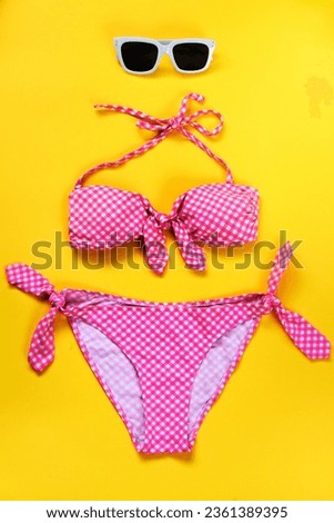 Top view of two pieces pink chequered swimming suit and white sunglasses over yellow background.