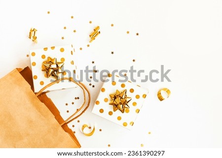 Top view of golden dotted gift boxes, a shopping bag and star shaped golden confetti on a white background. Copy space.