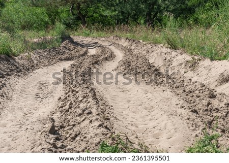 Sand road in the forest. Tire pattern of quad bike on driveway. Track imprint of quadricycle on nature land. Sand texture off road. Path in forest close up. Sand mounds and green forest in sunny day. Royalty-Free Stock Photo #2361395501