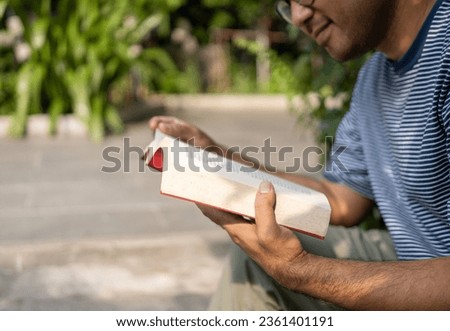 Close-up male hands opening reading and relaxing a book on relax time at nature park. Vacation time of man holding book turning the page sitting at nature background.