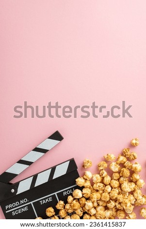 Movie Magic Display: Vertical top view of popcorn and a clapperboard on a pastel pink surface, providing space for your text or promotional message