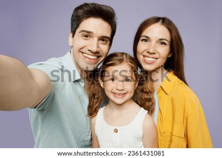 Close up young happy parents mom dad with child kid daughter girl 6 year old wear blue yellow casual clothes do selfie shot pov mobile cell phone isolated on plain purple background Family day concept